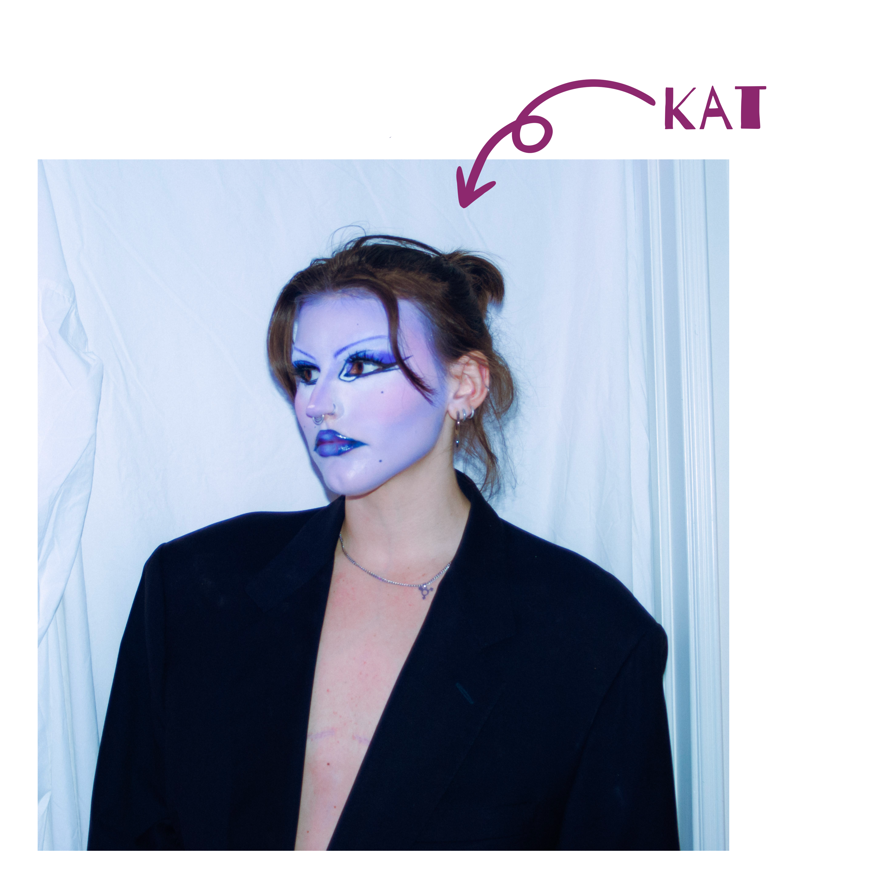 Kat, a white person with brown hair in a bun, looks off to the side against a white backdrop. They wear an oversized blazer open over a bare chest with visible top surgery scars, and bold purple makeup with blue eyeshadow and lip. A hand-drawn arrow labels them "Kat."
