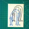 A rectangular art print featuring layered linocut design of a figure in a backbend in blue and black ink. Displayed on green cutting mat with grid lines.