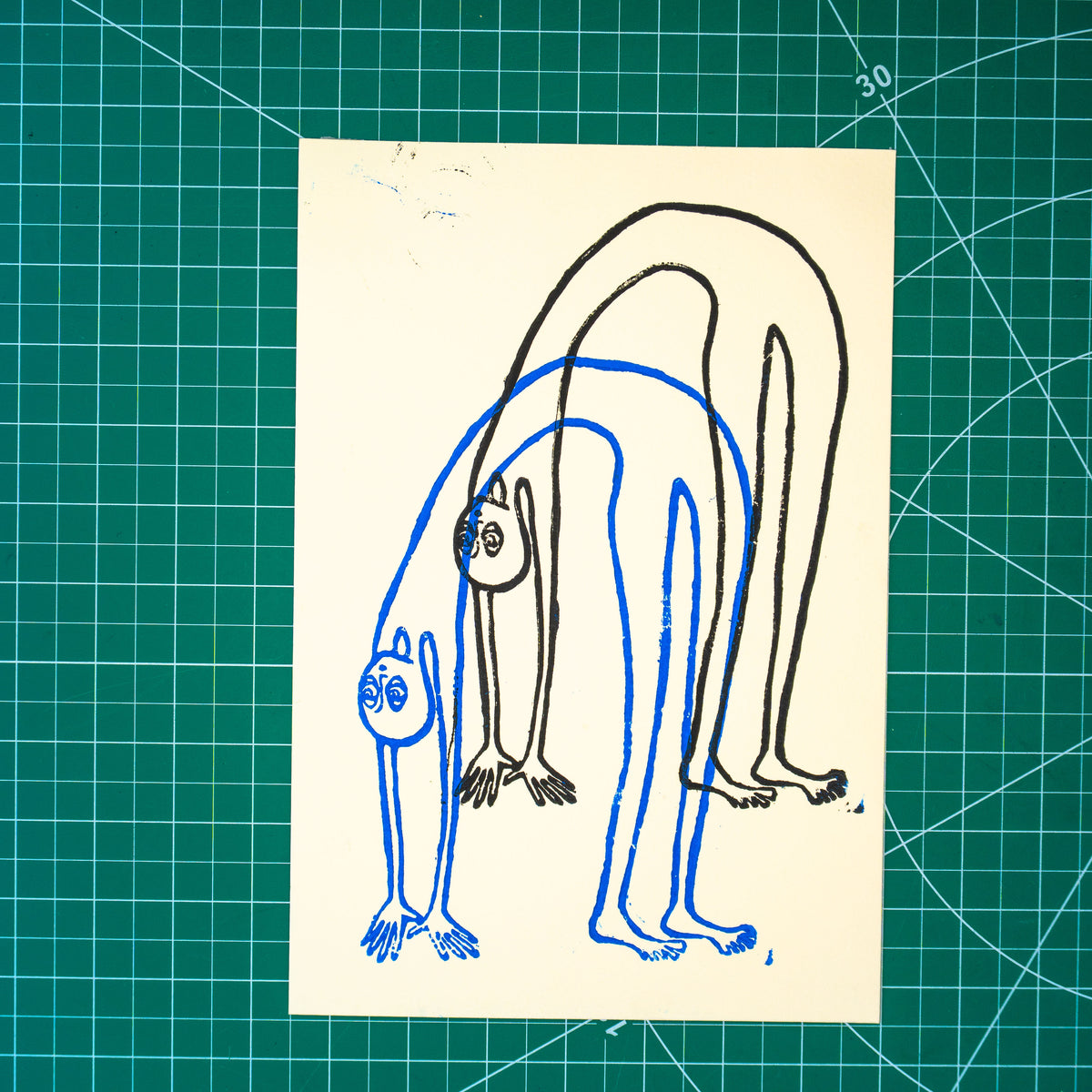 A rectangular art print featuring layered linocut design of a figure in a backbend in blue and black ink. Displayed on green cutting mat with grid lines.