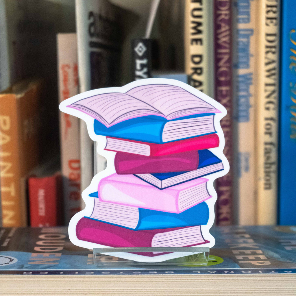 A large die-cut sticker shaped like a stack of colorful books, displayed on a bookshelf in front of blurred books.