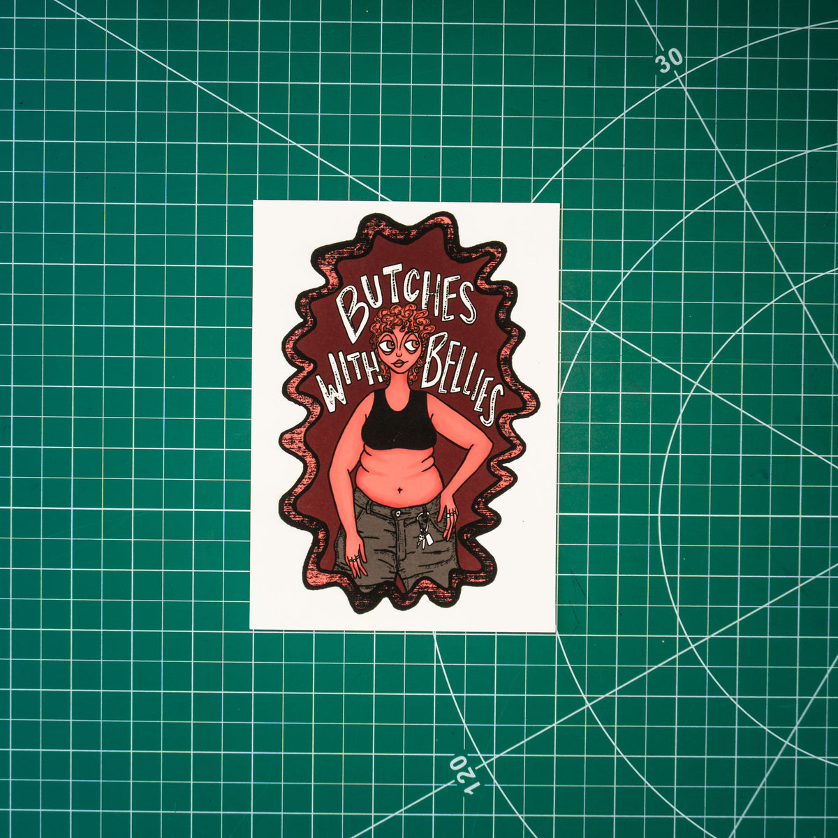 A small rectangular art print featuring an illustrated figure with a black sports bra, belly, and caribeener on jean shorts with the text "Butches with bellies" around them.