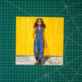 Colored pencil composition of a girl walking forward in a navy suit with billowing pants and a vest with a lapel. She has caramel-colored skin and dark brown hair, one hand in her pocket. A shadow falls across the gray floor beneath her, with a bright yellow wall behind.