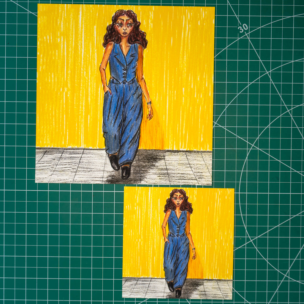 Two hand-drawn art prints of a woman in a blue jumpsuit walking against a yellow background, displayed on a green cutting mat.