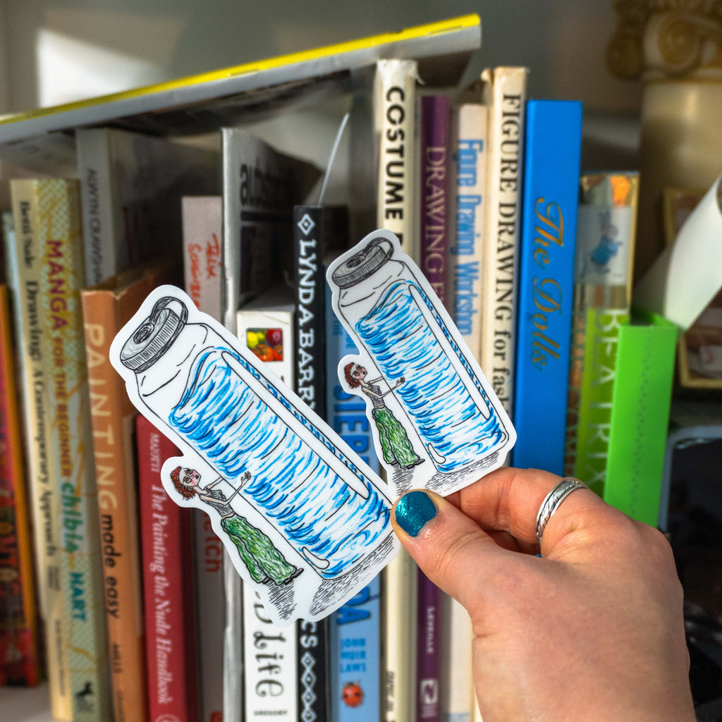 A hand with blue nail polish holding both variations of the Emotional Support Bottle sticker in front of a bookshelf.