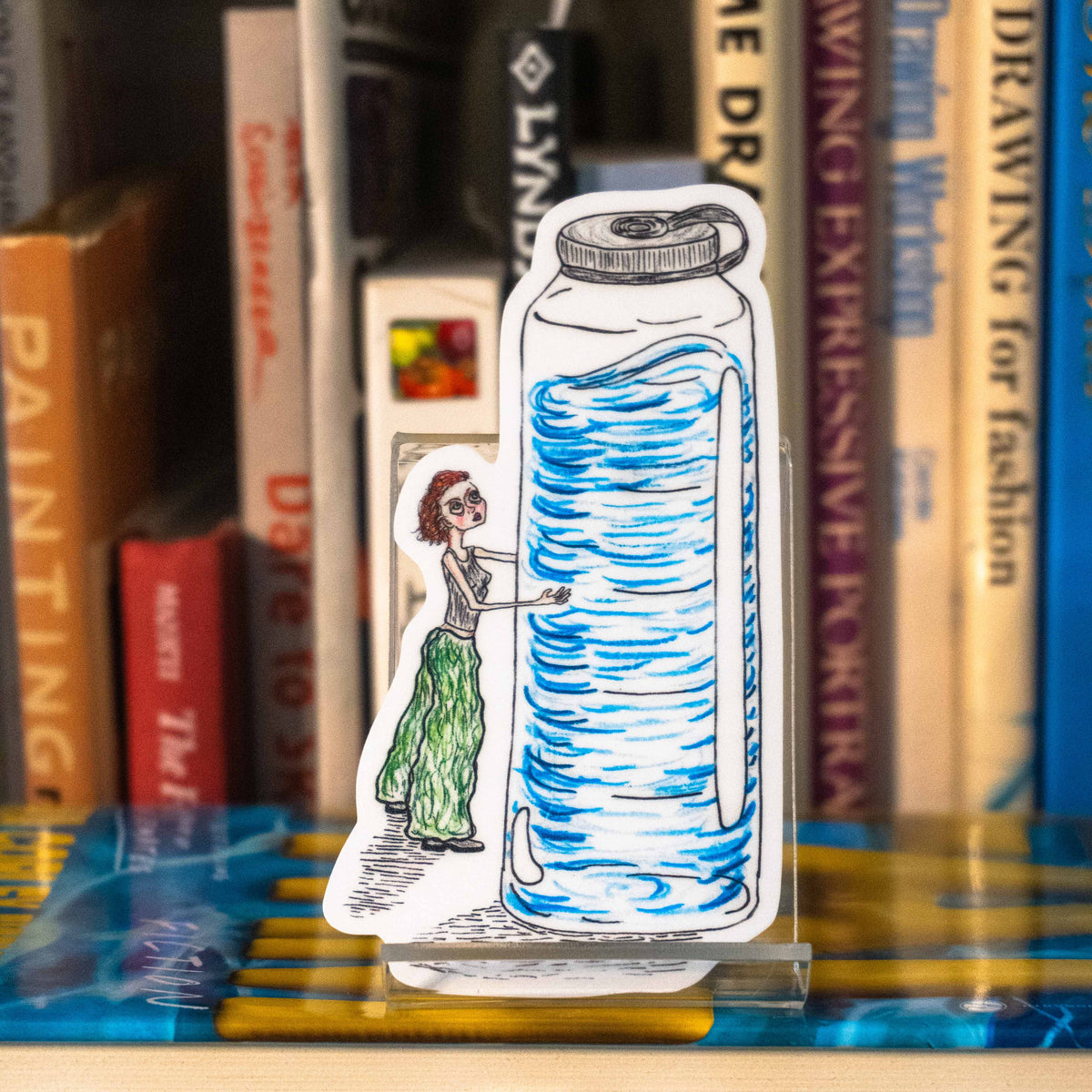 A large die-cut sticker featuring an illustrated figure hugging a waterbottle that is twice her size displayed on a clear acrylic stand in front of a bookshelf.