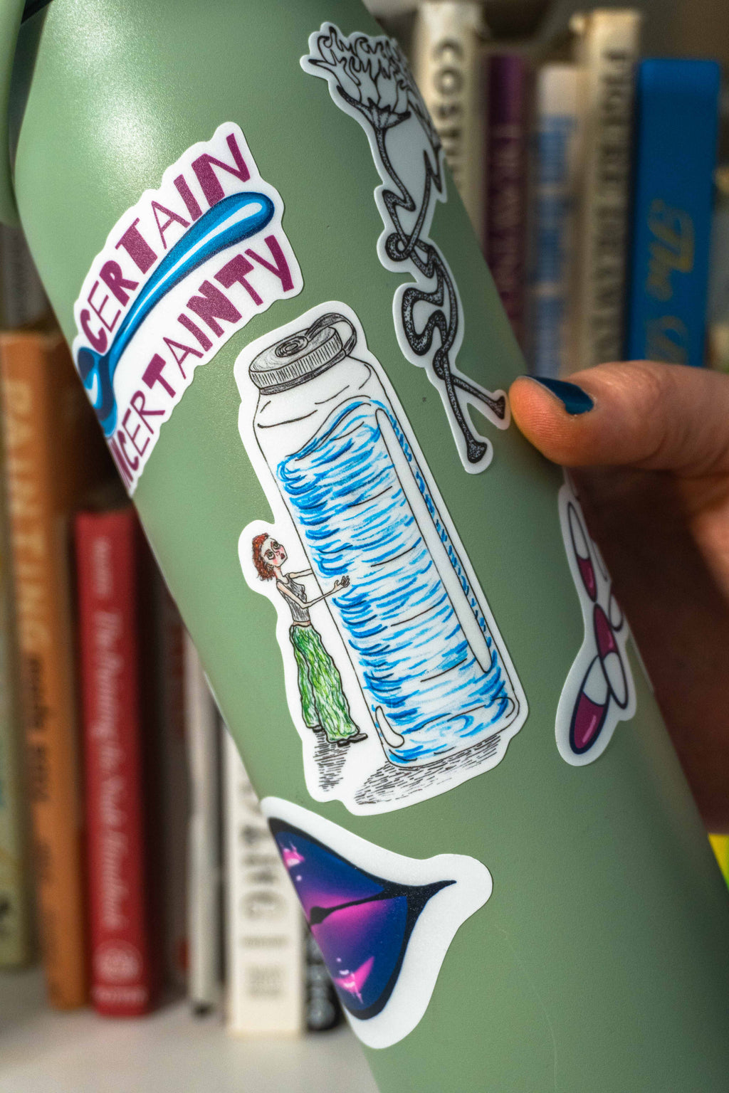 A close-up of a sage green insulated tumbler covered in colorful stickers with the emotional support bottle die cut sticker in the center. 