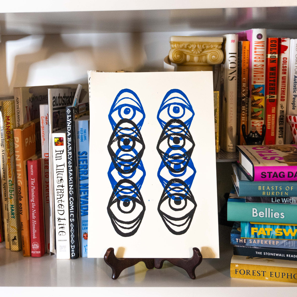 Eye Lino print displayed on a wooden easel  in a bookshelf.