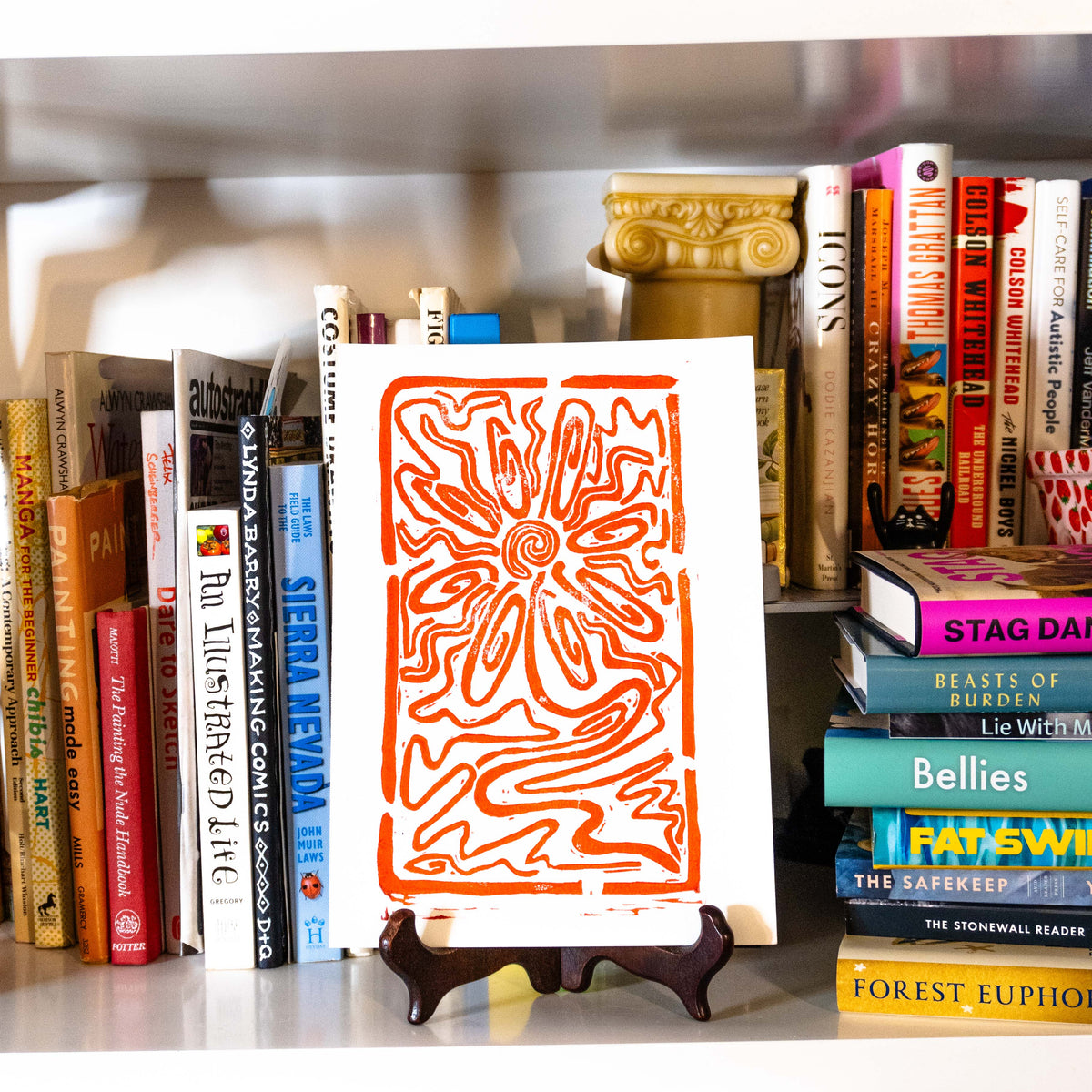 Flower lino print displayed on shelf filled with books.