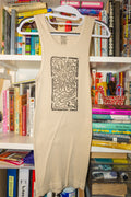 A beige tank top with a black rectangular linocut flower print hanging on a white hanger in front of a bookshelf filled with books.