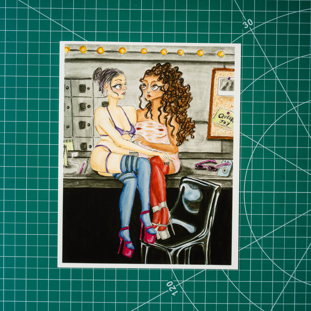 Gouache and watercolor painting of two feminine-presenting people embracing while seated on a counter. A mirror behind them reflects the scene and holds a bulletin board with a note reading “Queer Joy.” Both figures wear high heels, stockings, and thick eyeliner.