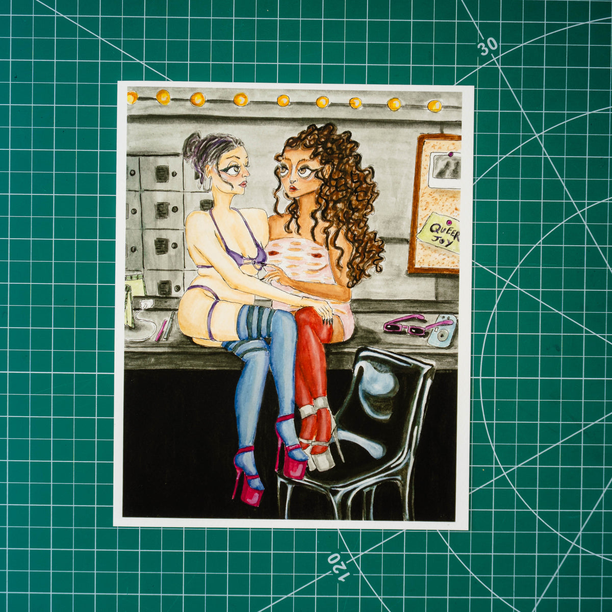 Gouache and watercolor painting of two feminine-presenting people embracing while seated on a counter. A mirror behind them reflects the scene and holds a bulletin board with a note reading “Queer Joy.” Both figures wear high heels, stockings, and thick eyeliner.