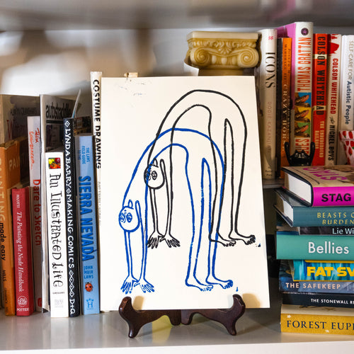 Multicolor Bendy guy linocut print displayed on an easel in a bookshelf.