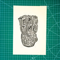 A square cream-colored art print featuring a black ink linocut illustration of a teapot and the words 'TEA TIME', displayed flat on a green cutting mat with grid lines.